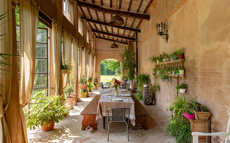 Le Limonaie di Villa Malaspina. Interno con tavolo aparrecchiato elegantemente e decoarato con fiori e piante.